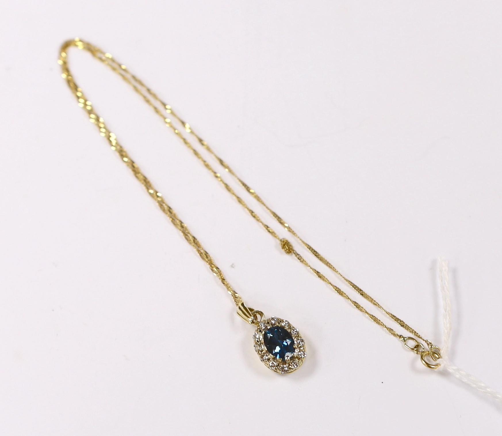A yellow metal, blue topaz and diamond set oval cluster pendant, 11mm, on a 375 fine link chain, 38cm, gross weight 3 grams.